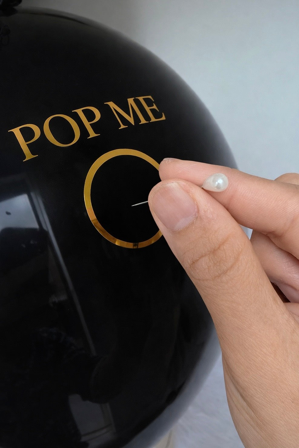 Black balloon with 'POP ME' text and a hand holding a needle.