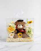 Graduation-themed teddy bear with flowers in a clear gift bag, full product view