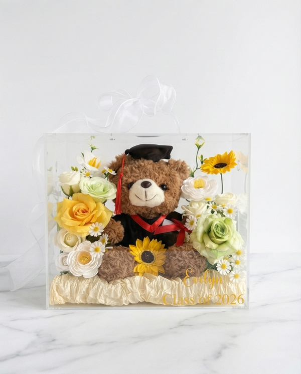 Graduation-themed teddy bear with flowers in a clear gift bag, full product view