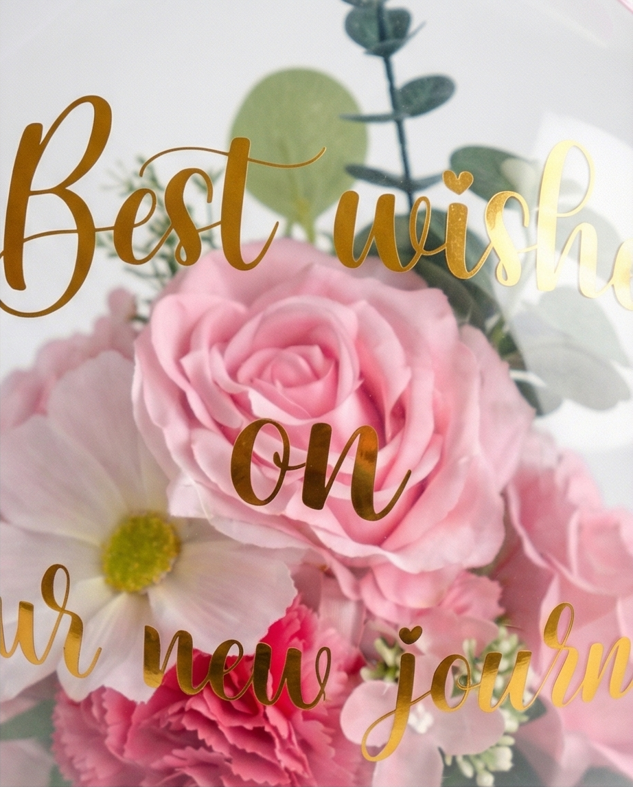 Pink floral arrangement in a transparent dome with 'Best wishes on your new journey' text, text close up