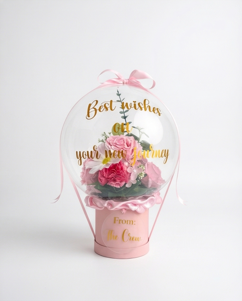 Pink floral arrangement in a transparent dome with 'Best wishes on your new journey' text, full product view