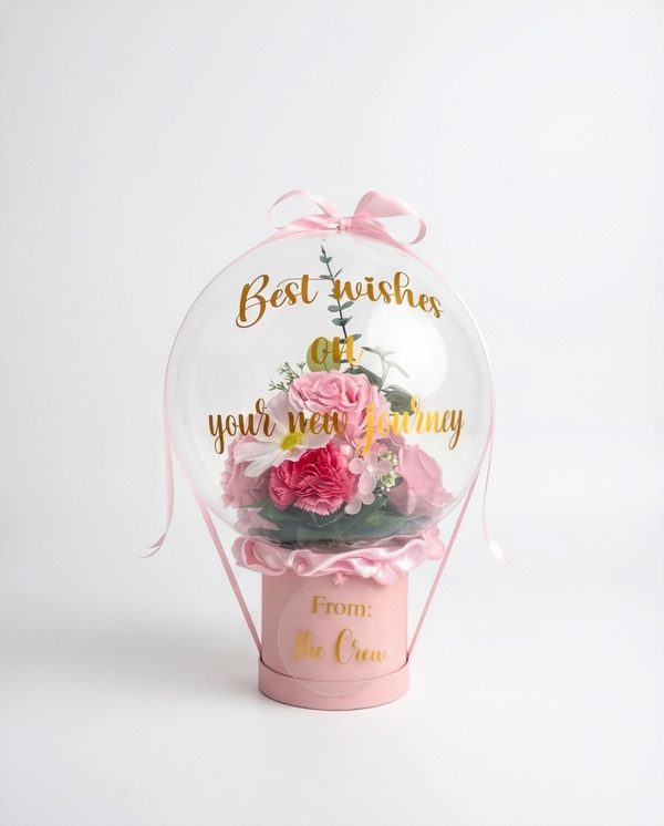 Pink floral arrangement in a transparent dome with 'Best wishes on your new journey' text, full product view