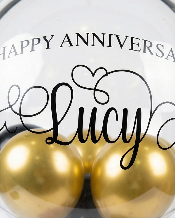 Decorative balloon with gold balloons, teddy bear, and red roses inside a clear dome, text close up