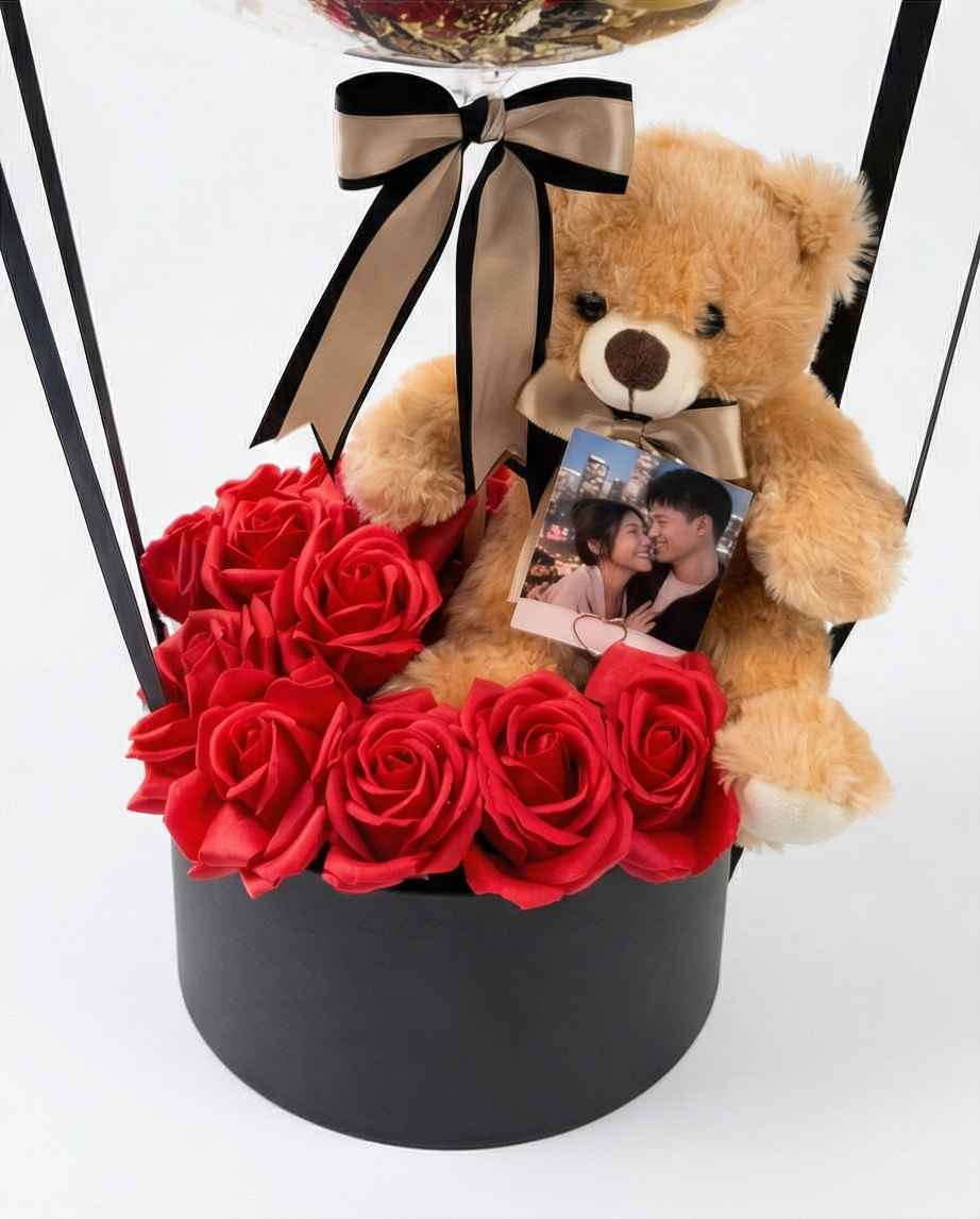 Decorative balloon with gold balloons, teddy bear, and red roses inside a clear dome, teddy bear and flowers close up