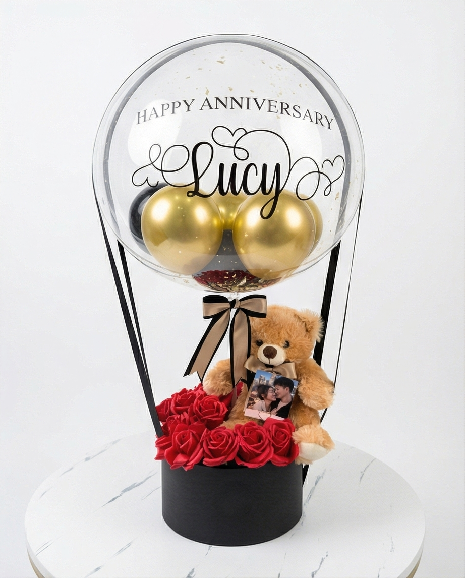 Decorative balloon with gold balloons, teddy bear, and red roses inside a clear dome, full product view