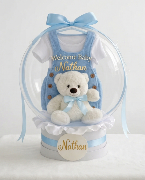 Baby gift set with teddy bear, blue romper, and 'Welcome Baby' text in a clear dome, full product view