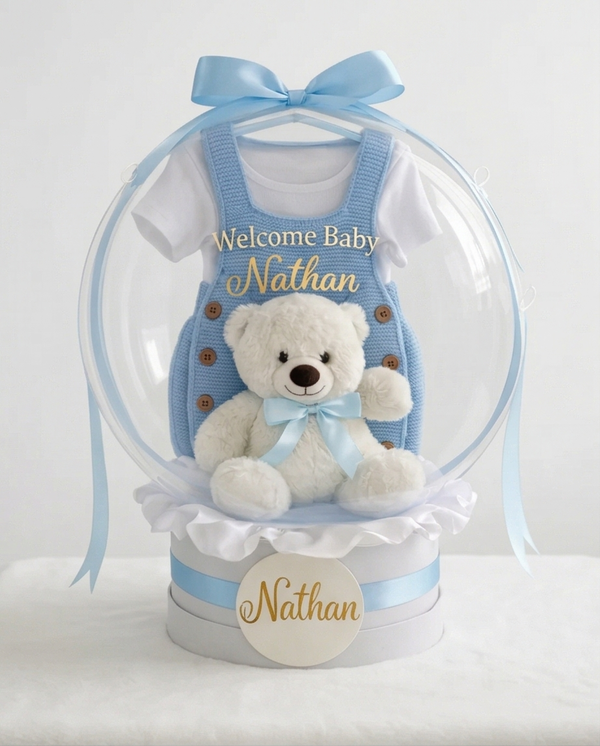 Baby gift set with teddy bear, blue romper, and 'Welcome Baby' text in a clear dome, full product view
