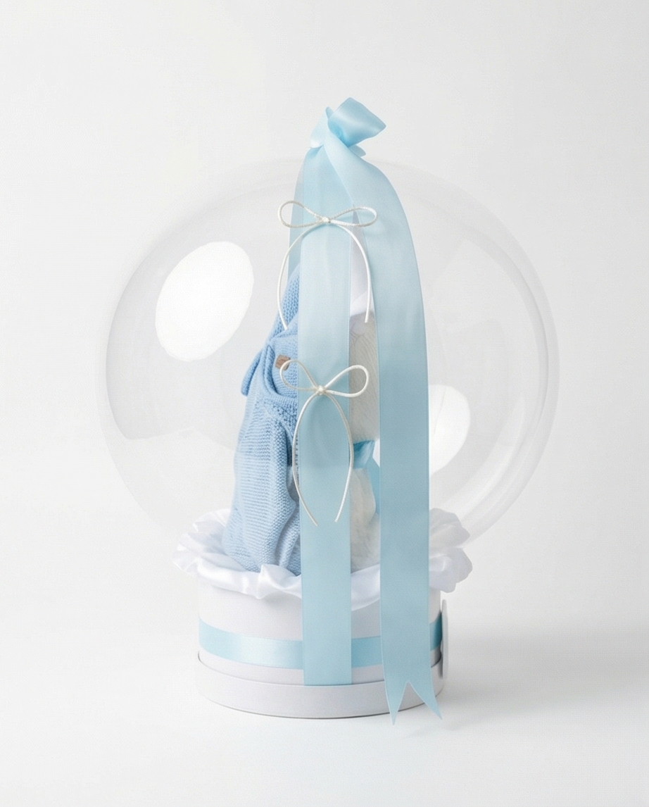 Baby gift set with teddy bear, blue romper, and 'Welcome Baby' text in a clear dome, side view